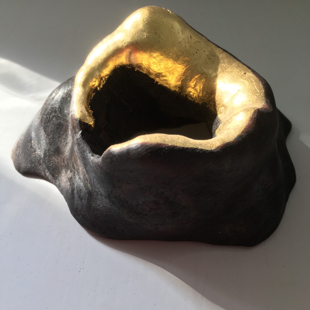 photograph of a sculpture of a piece of found wood with a gold gilded rim in the shape of a new moon